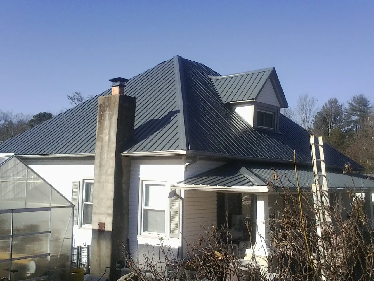 Dark blue standing seam metal roof on a white farmhouse with dormer — Slate & Tile Roof Repair by Roofing Brothers in Sparr
