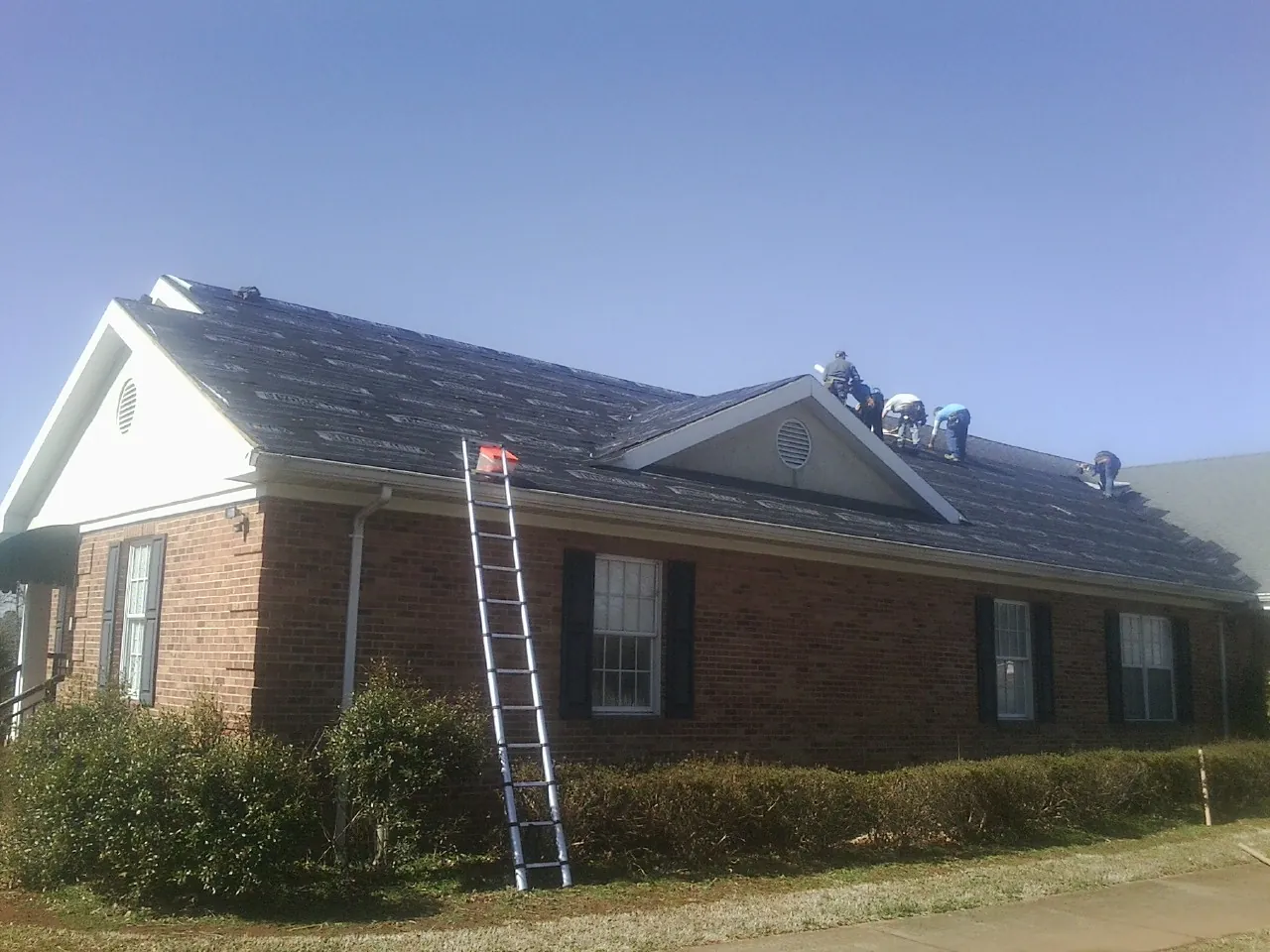 Crew tearing shingles off a brick ranch roof with a ladder set — Emergency Roof Repair work by our crew in Sparr