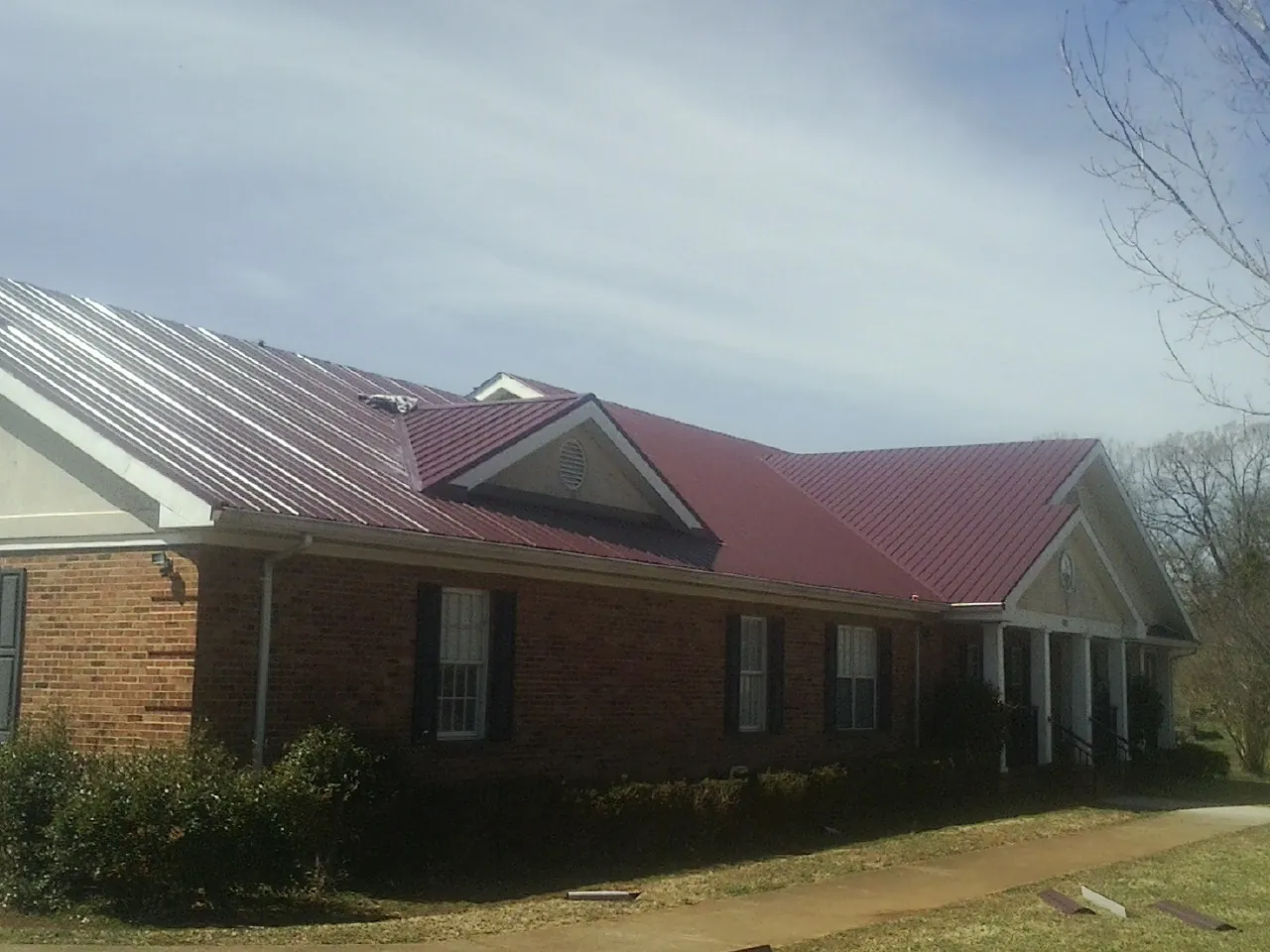 Red metal roof with gabled entries on a long brick building, from a Hail Damage Roof Repair job in Sparr