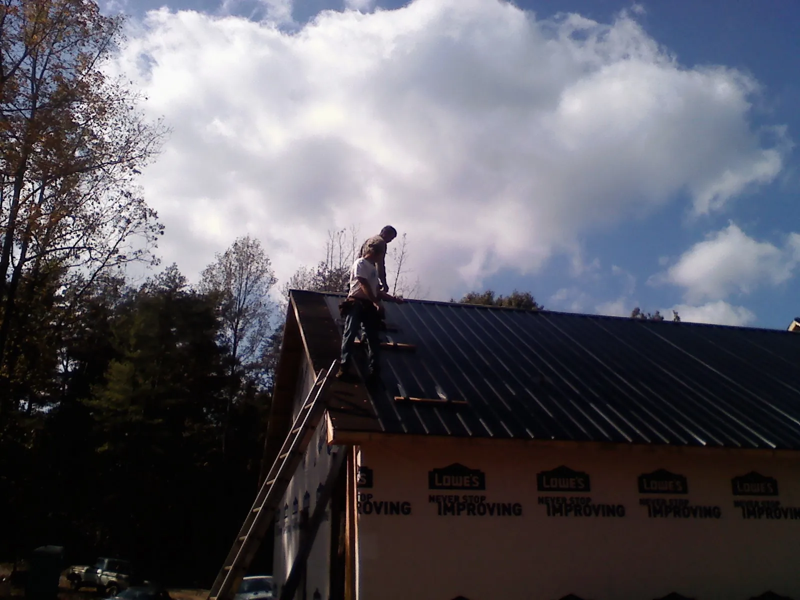 Roofer fastening dark metal panels high against a cloudy sky, from a Roof Inspection job in Sparr